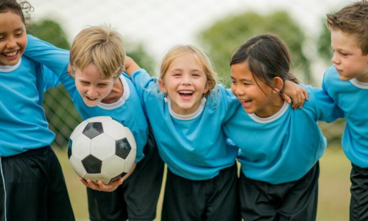 Kids laughing, linking arms, holding a soccer ball.